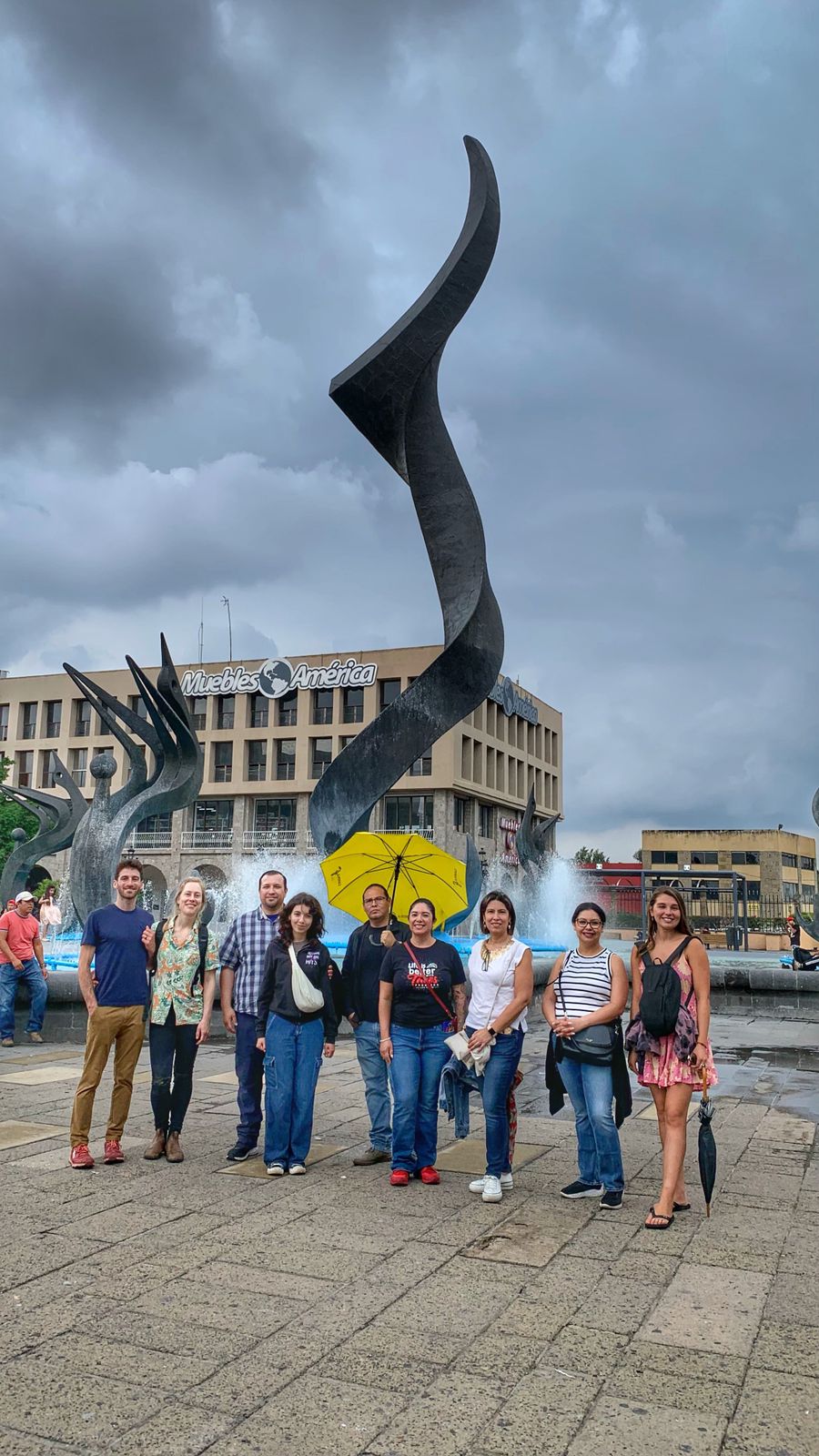 Grupo frente a escultura en plaza pública nublada.