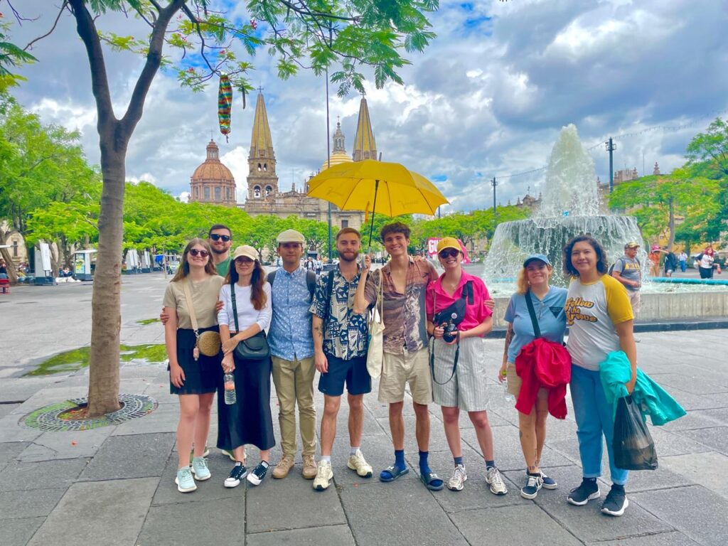 Grupo de personas en plaza con fuente y catedral.