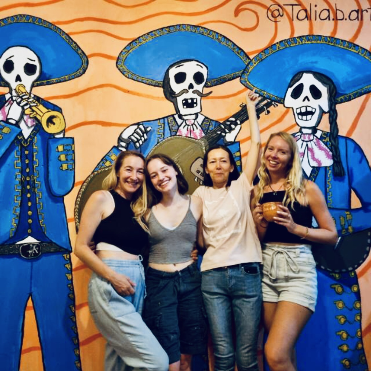 Mujeres frente a mural de catrinas mariachi.
