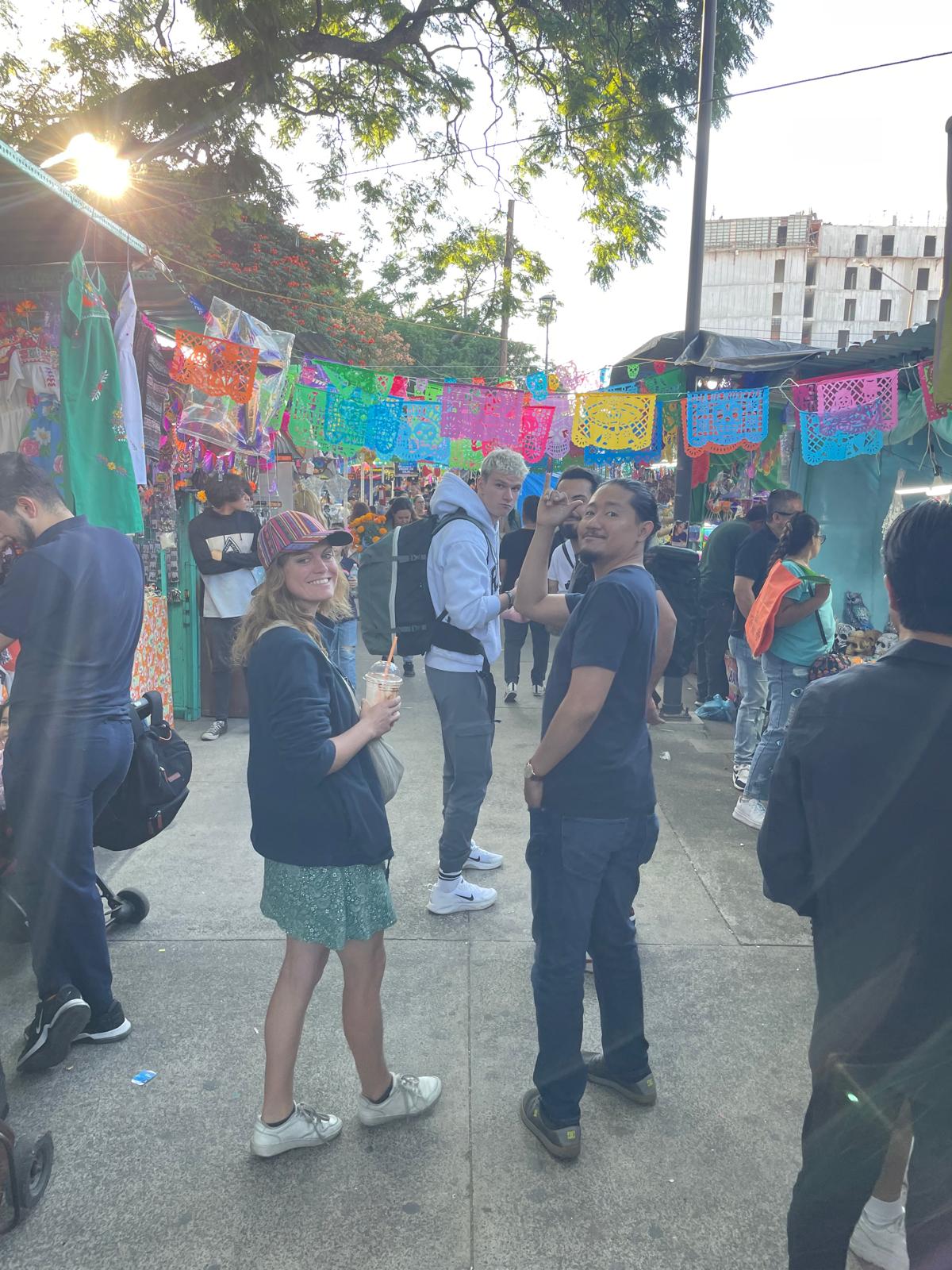 Personas paseando en mercado mexicano con papel picado colorido.