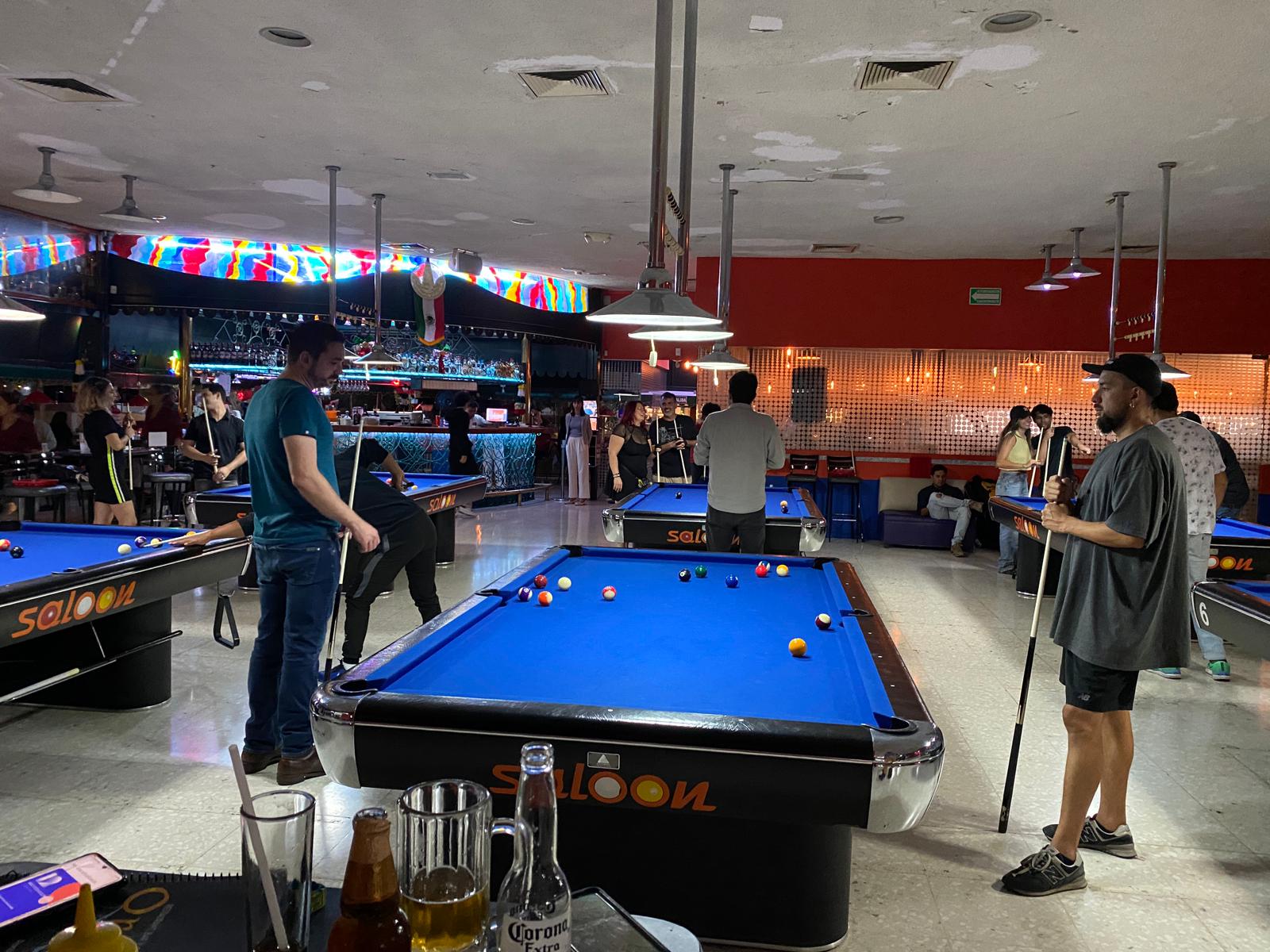 Personas jugando billar en un salón concurrido.